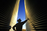 A man looks out from between two grain storage bins